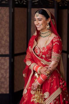 a woman in a red and gold bridal gown smiles at the camera while holding her hand on her hip