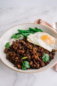 a white plate topped with meat and green beans next to an egg on top of it