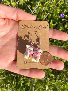 a person is holding a penny and two small cow earrings in front of some bushes