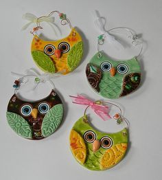 four ceramic owl ornaments hanging from hooks on a white surface, each decorated with an ornament