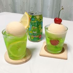 two glasses filled with green liquid and ice cream next to a can of soda on a table