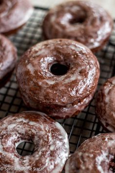 chocolate donuts cooling on a wire rack with icing sprinkled around them