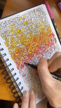 a person is drawing with colored pencils on a paper that has yellow and red squares