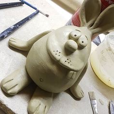 a clay bunny sitting on top of a table next to paintbrushes and glue