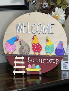 a welcome sign on top of a table with chickens and chicks in the nest below it