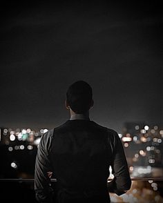 a man standing on top of a roof looking out at the city lights in the distance