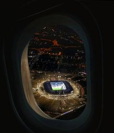 an airplane window with the view of a stadium from it's seat area at night