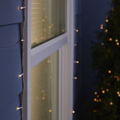 christmas lights are hanging on the side of a house in front of a lit up tree