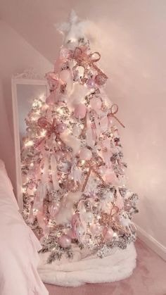 a white christmas tree with pink and silver ornaments on it's base in a bedroom