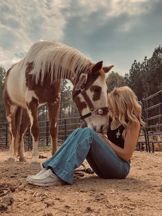 a woman sitting on the ground next to a horse