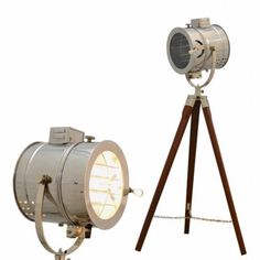 an old fashioned spotlight light next to a tripod lamp on a wooden stand with a white background