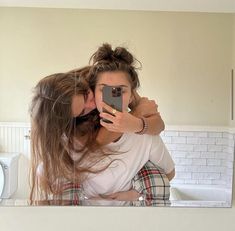 two women taking a selfie in front of a bathroom mirror with the reflection of them