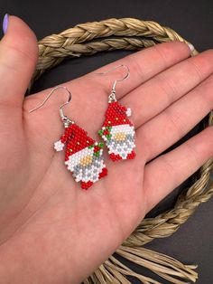 a pair of red and white beaded santa claus earrings on a person's hand