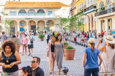 many people are walking around in the city square, and one person is taking pictures with her cell phone