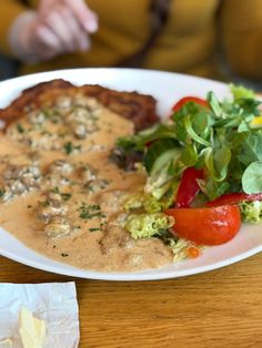 a white plate topped with meat covered in gravy and veggies next to a salad