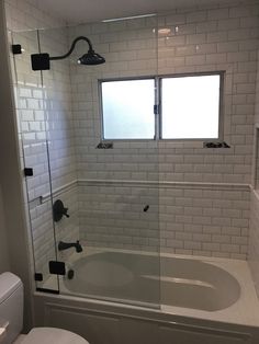 a bathroom with a tub, toilet and window in the shower stall that has glass doors on both sides