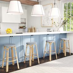 a kitchen with blue cabinets and stools in front of the counter top, along with three hanging lights