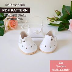 a pair of white baby shoes sitting on top of a table next to pink flowers