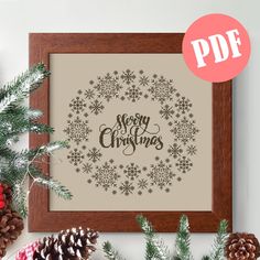 a cross - stitch christmas wreath with pine cones and evergreen needles is displayed in front of the frame