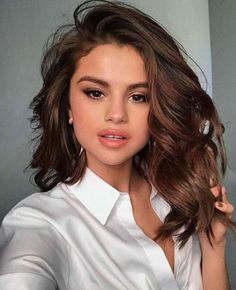 a woman with long brown hair wearing a white shirt and gold hoop earrings