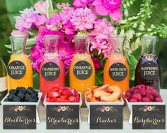 an assortment of juices and fruit in containers on a table with flowers behind them