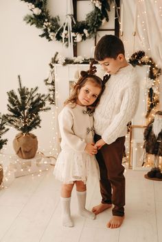 a young boy and girl standing next to each other in front of christmas tree with lights