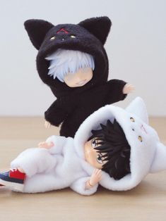 two dolls are dressed in black and white clothing, one is wearing a cat costume