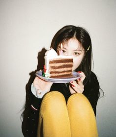 a woman holding a plate with a piece of cake on it in front of her face