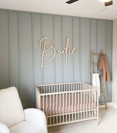 a baby's room with a crib, chair and wooden name sign on the wall