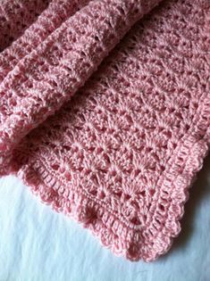 a pink crocheted blanket laying on top of a bed