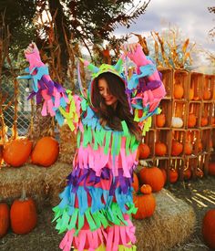 a woman in a colorful costume standing next to hay bales with pumpkins behind her