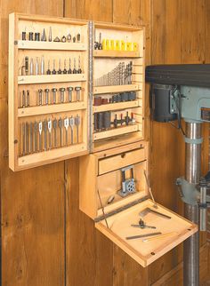 a workbench with many tools in it on a wooden paneled wall next to a drill press