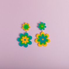 two pairs of colorful flower earrings on a pink background