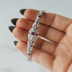 A lovely mid - late 20th century estate reproduction of a classic Art Deco bracelet motif. This beautifully intricate bracelet is set in 14k white gold and set with natural rubies and diamonds. In classic Art Deco style, the design features strong architectural structured lines in a symmetrical design mimicking the booming industry of the 1920's and 30's. The clasp of this bracelet features an additional safety lock to ensure a comfortable and secure fit. Luxury Ruby Diamond Bracelet, Luxury Ruby Diamond Bracelet For Formal Occasions, Art Deco Ruby Jewelry For Formal Occasions, Classic Ruby Tennis Bracelet For Formal Occasions, Elegant Red Bracelet With Diamond Accents, Elegant Ruby Tennis Bracelet For Formal Occasions, Elegant Red Bracelets With Diamond Accents, Elegant Red Diamond Bangle Bracelet, Elegant Ruby Diamond Bracelet For Formal Occasions