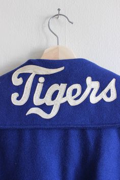 "Vintage Sweeney Sportswear varsity jacket in vibrant cobalt blue woven woolen type fabric with classic letterman jacket style boxy shape, sailor style collar, snaps down front, welt pockets at hips with blue leather-look trim, long sleeves, athletic-style blue, white, and purple stripe knit banded trim along cuffs and hem, off white satin appliqué 'Tigers' in script on back collar, full black quilted lining. Good vintage condition - some overall wear. full garment measurements: bust: 46\" waist Blue Sporty Outerwear For Game Day, Blue Outerwear With Baseball Collar For Sports Events, Blue Collegiate Varsity Jacket For Sports, Collegiate Blue Varsity Jacket For Sports, Collegiate Blue Outerwear For Game Day, Blue Outerwear With Letter Patch For Fall, Blue Varsity Outerwear With Letter Patch, Blue Collegiate Varsity Jacket For Sports Events, Blue Collegiate Style Varsity Jacket For Sports Events