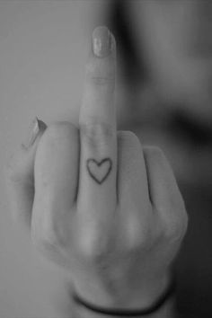 a woman pointing her finger at the camera with a heart tattoo on it's thumb