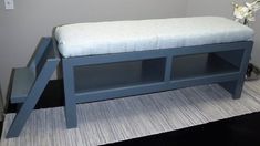 a blue bench with a white cushion on it in front of a gray wall and carpeted floor