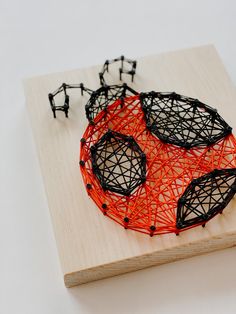 an orange string art piece sitting on top of a wooden board next to small black plastic figures