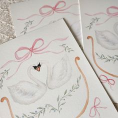 two cards with watercolor paintings of swans on them, one has a butterfly and the other has a bow