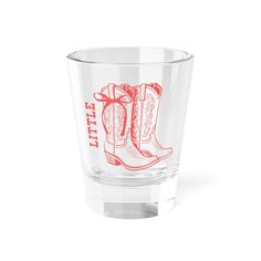 a shot glass with cowboy boots drawn on the side and red lettering that says little