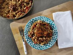 a blue and white plate topped with food next to a pan filled with chicken, rice and vegetables