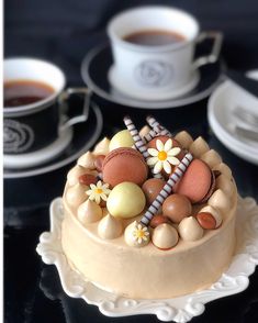 there is a cake decorated with eggs and other things on the table next to coffee cups