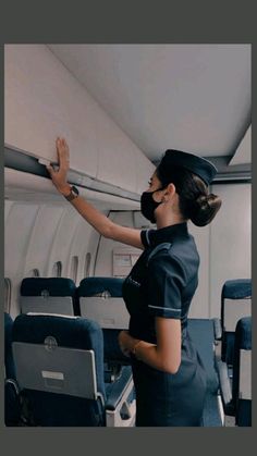 a woman wearing a face mask is standing on an airplane with her hands in the air