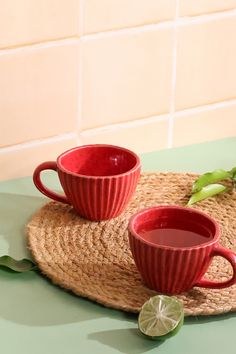 two red coffee cups sitting on top of a green table next to a slice of lime