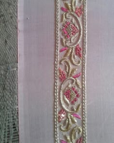 an embroidered ribbon with pink flowers and gold trimmings on a white fabric background