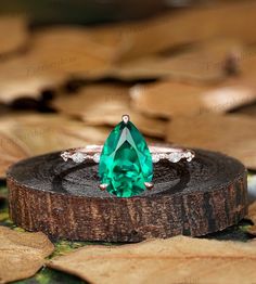 an emerald colored ring sitting on top of a piece of wood with leaves around it