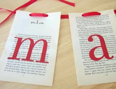 two bookmarks with the letter m on them are hanging from a red ribbon that is attached to a wooden table