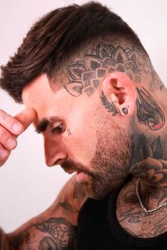 a man with tattoos and piercings on his head is looking at the camera while holding his hand to his ear