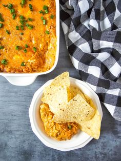 two white bowls filled with chicken enchiladas next to tortilla chips