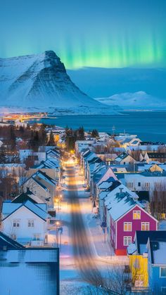 the aurora bore is seen over houses and mountains in this wintery town with snow on the ground